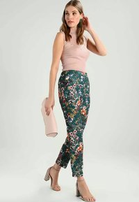 Cvečne zelene hlače imajo prilegajoč se kroj z zapletenim cvetličnim vzorcem in visokim pasom. Usklajene so z rožnatim rebrastim topom in »clutch« torbico.