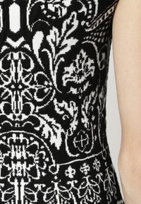 Garbino a maglia in bianco e nero con motivi floreali e geometrici intricati. Texture liscia con forma aderente, senza maniche.