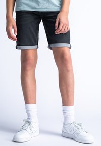 Pantalones cortos de mezclilla en un lavado oscuro con dobladillos enrollados, combinados con zapatillas deportivas blancas y calcetas. Textura mínima y diseño clásico de cinco bolsillos.