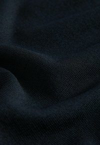 Černá texturovaná tkanina s měkkým, tkaným vzhledem. Materiál vypadá hladce a má jemný matný povrch, který ukazuje mírné záhyby.