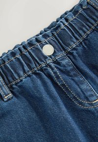 Modra jeans pas z nabranimi volančki in srebrnim kovinskim gumbom. Ima kontrastno rumeno šivanje in gladko teksturo tkanine.