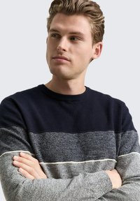 Marineblaue Strickpullover mit strukturiertem Oberteil und heller grauer gestreifter unteren Sektion. Verfügt über einen runden Ausschnitt und kontrastierende Nähte.