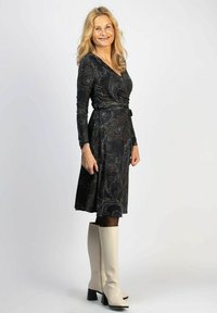 Musta mekko paisley-kuvioilla, pitkät hihat ja sidottu vyötärö. Yhdistetty polven korkeisiin valkoisiin saappaisiin, joissa on paksu korko.