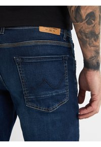 Tmavě modré džínové kalhoty se zlatým prošíváním, s charakteristickým designem zadní kapsy a koženou visačkou na pase.