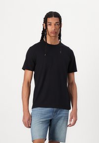 T-shirt de algodão preto com mangas curtas e decote redondo, combinado com calções de ganga claros. O tecido parece suave, com uma textura lisa.