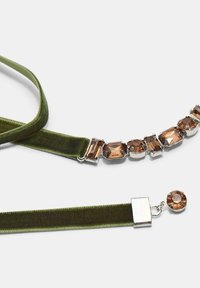 Zelený zamatový náhrdelník s obdĺžnikovými a oválnymi hnedými drahokamami zasadenými v kove. Obsahuje zapínanie s dekoratívnym akcentom z drahokamu.
