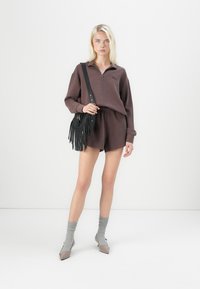 Brun zip-up genser med ribbete tekstur, sammen med matchende brune shorts. Modellen holder en svart fransete crossbody-veske. Grå sokker og spisse hæler.