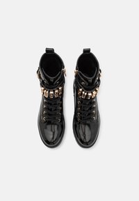 Bottines en cuir verni noir avec un design à lacets, accents en métal doré et un logo décoratif à l'avant. Doublure texturée.