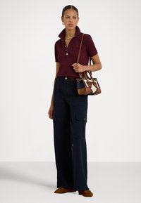 Μπορντό πόλο μπλούζα με κοντά μανίκια και γιακά, σε συνδυασμό με φαρδιά παντελόνια cargo σε ναυτικό μπλε. Καφέ τσάντα χειρός με διακοσμητικό σχέδιο και λεπτομέρειες.