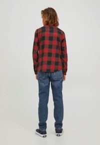 Röd och svart rutigt flanellskjorta, långärmad, ihopparad med blå denimjeans. Skorna inkluderar mörka sneakers med vita detaljer.