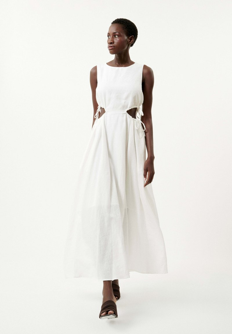 Robe maxi blanche sans manches en tissu léger, avec des découpes sur les côtés et des liens ajustables. Texture lisse avec une silhouette fluide.