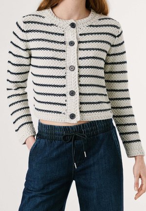 Witte gebreide cardigan met zwarte horizontale strepen en zwarte knopen, gecombineerd met donkerblauwe denim broek met koordje.