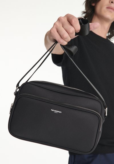 Melnas neilona plecu soma ar divām ar rāvējslēdzēju slēdzamām kabatām, gluda tekstūra, regulējama siksna un smalka "THE KOOPLES" zīmola atzīme baltā krāsā.