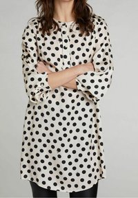Blusa di tessuto bianco con grandi pois neri, con bottoni frontali e maniche a tre quarti. Tessuto liscio, vestibilità comoda e tutto curvo.