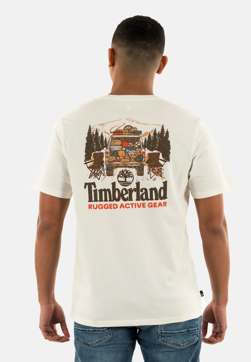 Camiseta de algodón color beige claro con un colorido gráfico de una furgoneta aparcada, árboles y sillas de campamento, con el texto "Timberland Rugged Active Gear" debajo.