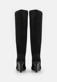 Bottes noires jusqu'aux genoux avec un haut en tricot ajusté, un design épuré, un bout pointu et un talon aiguille. Un tissu texturé recouvre la tige.