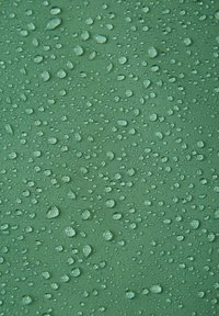 Wodoodporny zielony materiał o teksturowanej powierzchni, z licznymi kroplami wody, które podkreślają jego właściwości wodoodporne.
