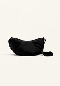 Czarna materiałowa torba o zakrzywionym kształcie, wyposażona w zamek błyskawiczny oraz teksturowany, plisowany design. Dołączony regulowany pasek.
