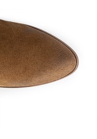 Zapato de ante marrón con punta redondeada y textura suave, que presenta un brillo sutil y una suela de cuero marrón oscuro delgada.