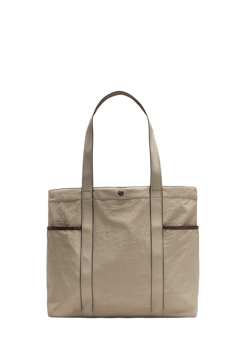 Bolso tote beige con tela texturizada, dos asas resistentes, bolsillo frontal con ribete marrón y diseño minimalista.