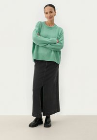 Pull en tricot vert menthe avec ourlet à côtes, associé à une longue jupe en denim noir avec une fente sur le devant et des chaussures noires.