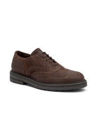 Scarpa in suede marrone con lacci, dettagli brogue e tomaia texturizzata, dotata di una suola in gomma nera spessa e punta arrotondata.