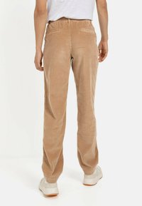 Lysebrune fløjlbukser med en afslappet pasform og elastisk talje. Synlig tekstur og sidelommer. Stylet med hvide sneakers.