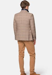 Brązowa marynarka w kratę o teksturowanym wykończeniu, z kontrastowym granatowym kołnierzem. Połączona z khaki chinosami i brązowymi zamszowymi butami.