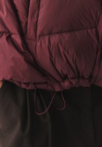 Bordeaux puffertjakke med en indsnævret elastisk talje, quiltet tekstur og en glat stoffinish med snørebåndsdetalje.