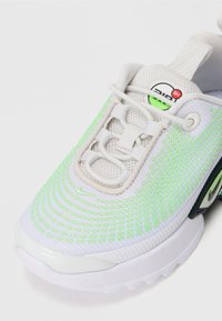 Sapatilha desportiva branca com parte superior em malha e detalhes em verde-neon, pormenores texturizados e um logótipo proeminente perto da lingueta.