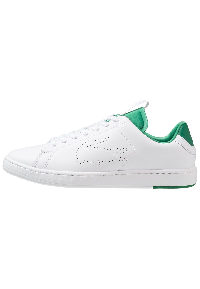 Baskets basses blanches avec doublure intérieure verte, logo crocodile perforé sur le côté, lacets blancs et semelle en caoutchouc blanche.