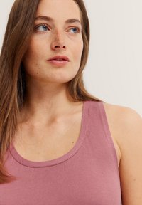 Light pink ribbed tank top with thin straps and a rounded neckline, featuring a soft texture and minimal seams.