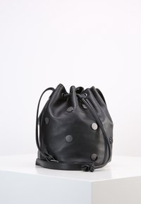 Borsa a secchiello in pelle nera con forma arrotondata, adornata da dettagli metallici a pois. Presenta una chiusura a fune e una tracolla regolabile.