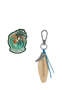 Coocazoo Schlüsselanhänger mit Ozean-Motiv, bestehend aus einem Surfbrett aus Holz mit eingraviertem Logo, silbernem Metallclip und einer blauen Kordelbefestigung. Inklusive runder Aufnäher.