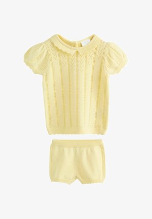 Gul strikket kortærmet top med en bølget krave og hjerte mønstre; kombineret med matchende gule shorts med elastisk talje.