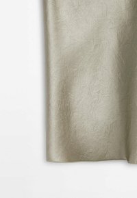 Tissu satiné beige clair avec une texture froissée subtile suspendu devant un fond blanc.