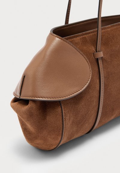 Καφέ τσάντα χειρός από σουέτ και δέρμα με στρογγυλεμένες άκρες και λεπτούς δερμάτινους ιμάντες σε λευκό φόντο.