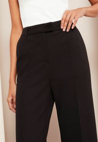 Zwarte high-waisted broek met een gestructureerde stof, een wijd been ontwerp, frontzakken en een strakke tailleband.