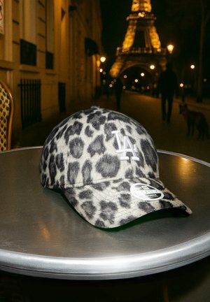 Cappellino da baseball LA con stampa leopardata su un tavolo di metallo di notte con la Torre Eiffel e pedoni sfocati sullo sfondo.