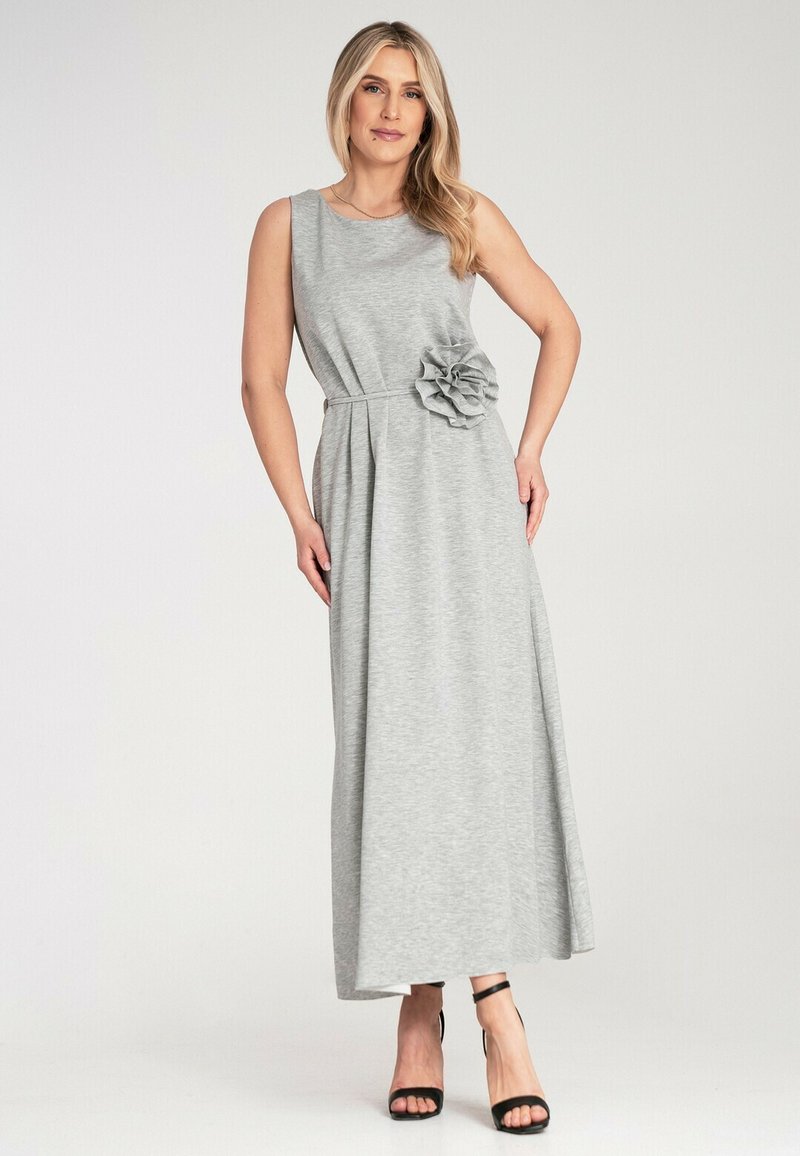 Szara, bezrękawnikowa maxi sukienka z kwiatowym akcentem w talii, wykonana z miękkiego materiału. Noszona z czarnymi sandałami na obcasie z paskami, o luźnym kroju.