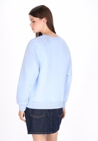 Világoskék pulóver kerek nyakkivágással, hosszú raglán ujjal és bordázott mandzsettákkal, farmer szoknyával párosítva, amelyen két hátsó zseb található.