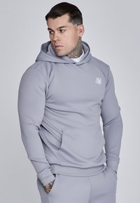 Gaiši pelēks kapuce, izgatavota no gludas auduma, ar priekšējo kabatu un mazu logo uz krūšu daļas. Tam ir klasiskā kapuces dizains ar auklu.