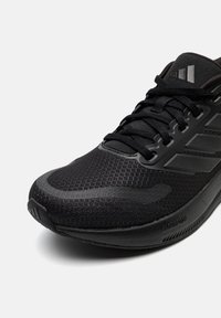 Close-up of a black athletic shoe with mesh upper, black laces, and three stripe design on the side on a white background.