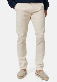 Pantalon en coton beige à coupe droite, doté de poches latérales, de légères plis et associé à des espadrilles gris clair.
