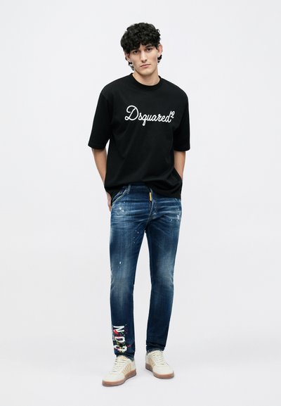 Black short-sleeve t-shirt with white "Dsquared²" logo, paired with blue denim jeans featuring paint splatter and colorful accents on the leg.