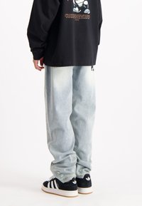 Lichtblauwe wijde spijkerbroek met rafelige details bij de zoom, gecombineerd met zwarte sneakers met witte strepen en logo-accenten.