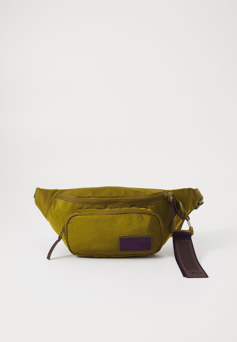 Olīvu zaļš fanny pack, kas izgatavots no teksturētas auduma, ar galveno rāvējslēdzēja nodalījumu, priekšējo kabatu un purpura krāsas logo plāksnīti un siksniņas akcentu.