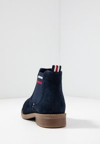 Bot�ín de ante azul marino con panel lateral elástico, tacón de madera marrón y tira de agarre en rojo, blanco y azul a rayas.