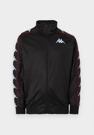 Črna trenirka z zadrgo spredaj, z belimi logotipi na prsih in obrokavnicah, s rdečim robom od ovratnika do manšet.