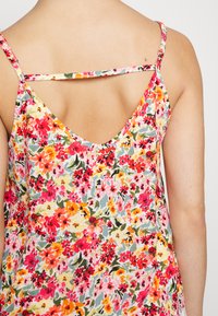 Vestido floral com um design às costas em V, apresentando padrões coloridos de flores vermelhas, cor-de-rosa, laranjas e verdes sobre um fundo claro. Alças ajustáveis.